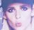 Pixelated close-up of a person's face with light skin, dark hair, and blue eyes against a gradient background.