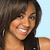 A pixelated close-up of a smiling person with dark hair and a black sleeveless top against a light blue background.
