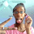 A person in a pink shirt with glasses and a raised hand gesture against a light blue background with white spots.