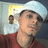 A pixelated static image shows a person in profile wearing a red shirt and dark cap, with a blurred background containing light blue and yellow shapes.