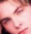 Pixelated close-up of a person's face with pink and brown tones, showing partial eyes, nose, mouth, and dark hair against a light background.