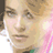 Pixelated close-up of a person's face with light brown hair, pink-tinged cheeks, and a green garment visible at the bottom edge.