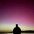 Silhouette of a figure with outstretched arms against a gradient sky transitioning from purple to yellow.
