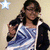 A person in a blue and white striped top with dark jacket holds up two fingers near their face, standing against a light background with a star symbol.