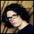 Pixelated static image of a person with dark hair and light skin, viewed from the side against a textured background.