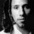 Black-and-white pixelated portrait of a person with long dark hair, wearing light-colored clothing against a solid black background.