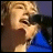 A person in a blue shirt sings into a black microphone with mouth open, visible text "JAMES" appears on the right