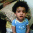 A pixelated image of a child with dark curly hair wearing a light blue shirt, standing in front of an indistinct background.
