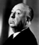 Black-and-white static icon of a bald man in profile wearing a dark suit and white shirt, with visible facial features including eyes, nose, mouth, and ear against a gradient background.