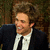Pixelated portrait of a person with light brown hair wearing dark suit, white shirt, and black tie against blurred background.