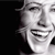 Pixelated grayscale image of a smiling face with closed eyes, partially cropped on the left side against a black background.