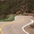 Pixelated image of a winding road with green grassy areas and brown terrain under a dark sky.