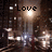 A nighttime cityscape with illuminated streetlights and blurred motion trails, overlaid with pixelated text reading "Love the City" in three separate segments.