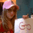 A person wearing a pink cap and red top holds up signs with changing text while smiling, set against a blue background.