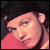 Pixelated static image of a person's face with dark hair and pinkish skin tones against a dark background, wearing a red garment.