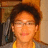 Pixelated portrait of a person with short dark hair wearing glasses and a yellow shirt against a blurred indoor background.
