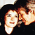Pixelated image of two figures in close proximity, one with light skin and reddish hair, the other with darker skin and brown hair, both facing forward against a dark background.