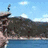 A person stands on a rocky cliff edge above water, then falls into the sea with a splash.