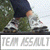 Static 50x50 pixel icon showing a person's lower body in motion, wearing dark shorts and white sneakers with red accents, standing on grassy terrain near a vehicle or structure.