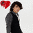 Pixelated image of a person with dark hair wearing a black outfit and gray jacket, standing beside a red heart symbol on a light background.