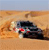 A pixelated image shows a dark vehicle on a sandy terrain with a light blue sky background.