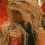 Two side-by-side figures with long blonde hair, wearing dark tops against a red background; one figure holds an object near their face.