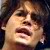 Pixelated close-up of a person's face with light skin tone, dark hair, and open mouth showing teeth, set against dark background.