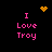 Pixelated text "I Love Troy" in pink appears on a black background with animated yellow pixel symbols above and below the text.