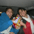 Two people in blue and red clothing hold a colorful object with yellow, white, and red patterns against a dark background.