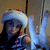 A person wearing a white Santa hat with red trim and blue gloves makes a peace sign with their right hand against a beige wall background.