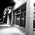 Black-and-white pixelated image of a figure in a hat holding a glowing object near a building with a triangular roof.