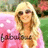 A static image shows a person with long blonde hair wearing sunglasses and a pink outfit, standing in front of green foliage and pink flowers.
