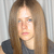 A pixelated close-up of a person with long light brown hair wearing a dark top against a striped background.