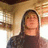 Pixelated static image of a person with long dark hair wearing a dark top against a blurred background with warm tones.