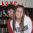 Two people stand close together under red pixelated text reading LOVE... with a blurred background of dark and light tones.