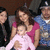 A group of people including a woman in pink holding a baby in pink, a man in blue, and a police officer, with a gray area on the right side.