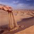 Pixelated desert landscape with rocky formations under a blue sky, featuring warm brown and orange tones with dark shadows.