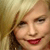 Pixelated close-up of a person with light hair and red lips smiling against a blurred background
