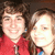Two people in a close-up photo with one wearing a red top, both with light brown hair, against a dark background.