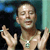 Static pixelated image of a shirtless man with raised hands against dark and teal background, wearing necklace with square pendant.