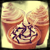 Three conical cups filled with swirled light brown dessert topped with dark brown drizzle, set against a soft yellow background with a dark border.