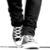 Black-and-white pixelated image of a person's lower legs and feet wearing dark pants and white sneakers with visible laces.