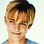 Pixelated close-up of a person with light brown hair, wearing a blue shirt against a white background.