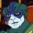 Pixelated static image of a character with blue and green hair, white face, and dark eye patches, set against a blurred background with red and brown tones.