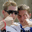 Two individuals in white and blue athletic shirts with red wristbands, one pointing at the other's face while wearing sunglasses.