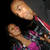 Two pixelated figures in close physical contact, one figure positioned above the other against a dark background.