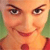 Pixelated close-up of a smiling person with light skin, brown eyebrows, and green hair, wearing a red garment with a circular detail.