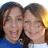 Two people with brown hair smiling closely together, one in blue clothing and the other in white, against a light background.