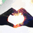 Six show hands forming a heart shape with changing backgrounds: white clouds, sunset, blue sky, grayscale, green, and purple sunset