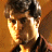 Pixelated close-up of a person with dark hair and light skin, wearing a dark top against a warm brown background.